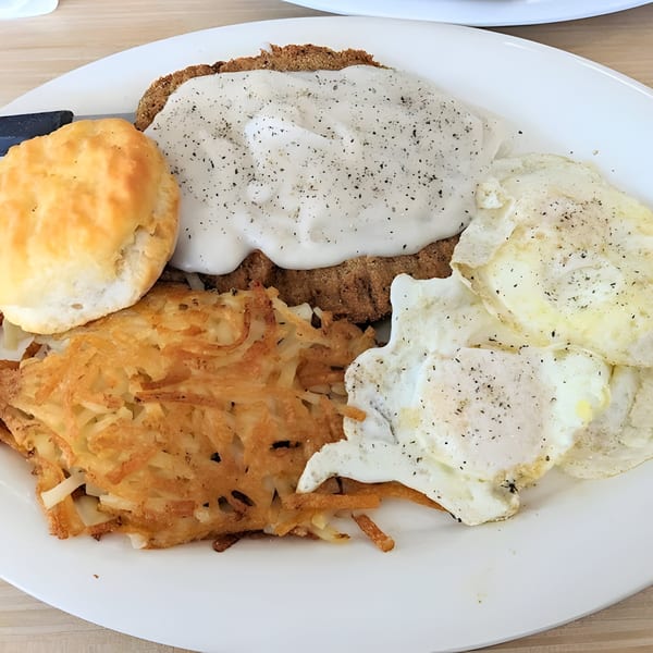 A breakfast plate with chicken fried steak, gravy, hash browns, two fried eggs, and a biscuit.