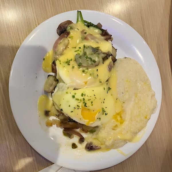 Eggs Benedict with hollandaise sauce, mushrooms, and grits on a white plate from That Flippin' Egg.