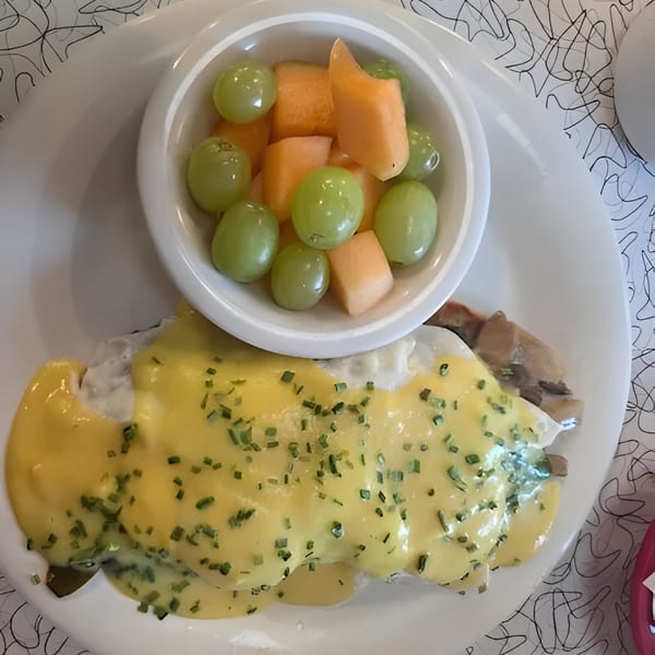 Eggs Benedict with hollandaise sauce and chives, served with a side of grapes and cantaloupe.