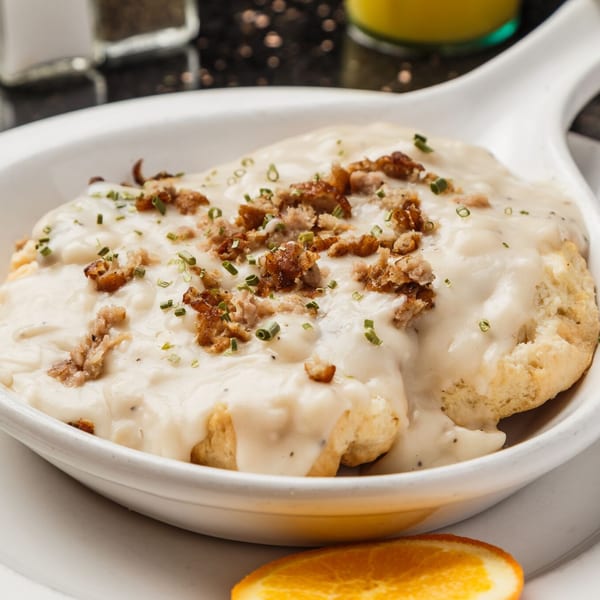 Biscuits and gravy topped with sausage crumbles and chives, served with an orange slice.