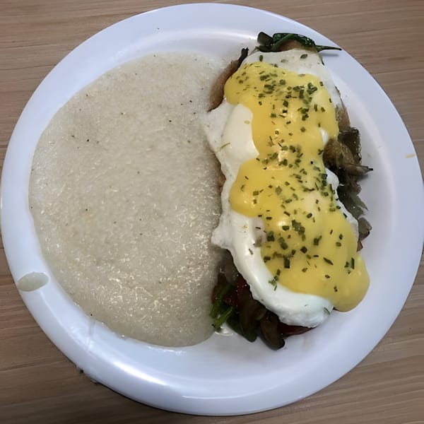 Creamy grits and eggs Benedict with hollandaise sauce and herbs on a white plate.