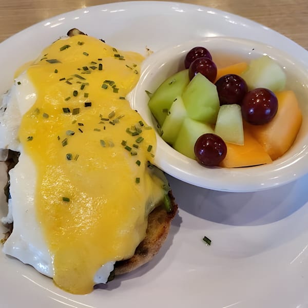 Eggs Benedict with hollandaise sauce and chives, served with a side of fresh fruit.