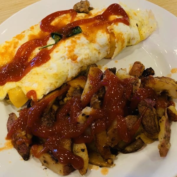 A breakfast plate with a ketchup-drizzled omelet and home fries from That Flippin' Egg.