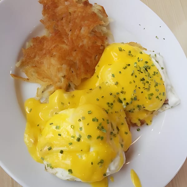 Eggs Benedict with hollandaise sauce and chives, served with crispy hash browns on a white plate.