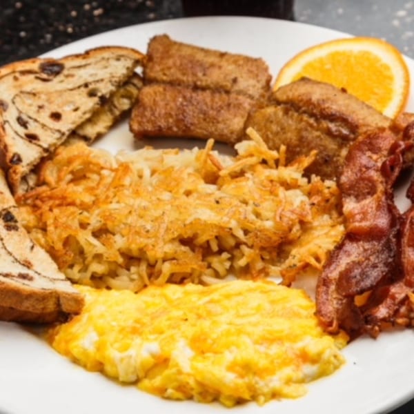 A breakfast platter with scrambled eggs, hash browns, bacon, cinnamon raisin toast, and French toast sticks.