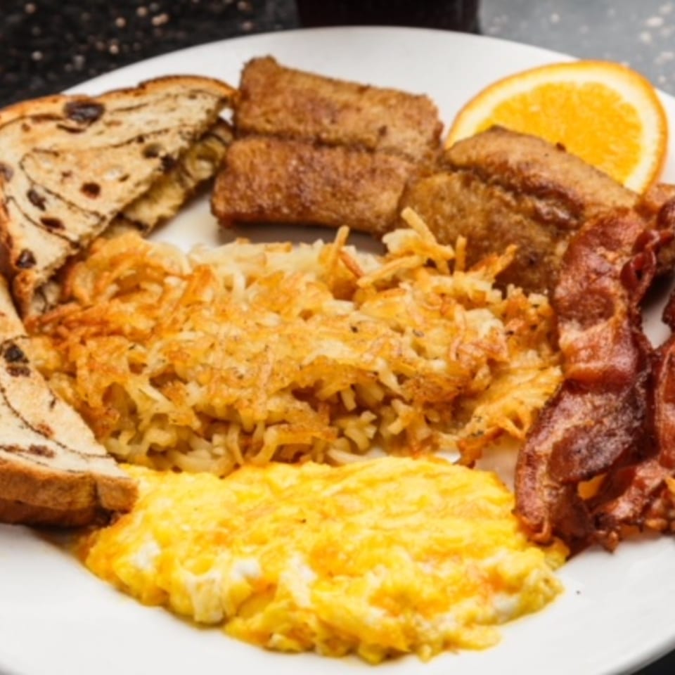 A breakfast platter with scrambled eggs, hash browns, bacon, cinnamon raisin toast, and French toast sticks.