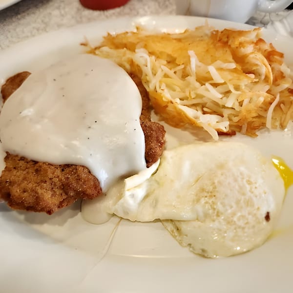 Chicken fried steak with gravy, hash browns, and a fried egg on a white plate.