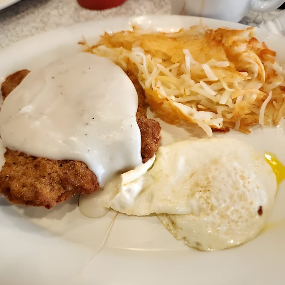 Chicken fried steak with gravy, hash browns, and a fried egg on a white plate.