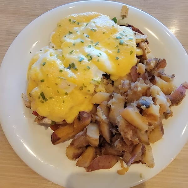 Eggs Benedict with hollandaise sauce and chives, served with roasted potatoes on a white plate.