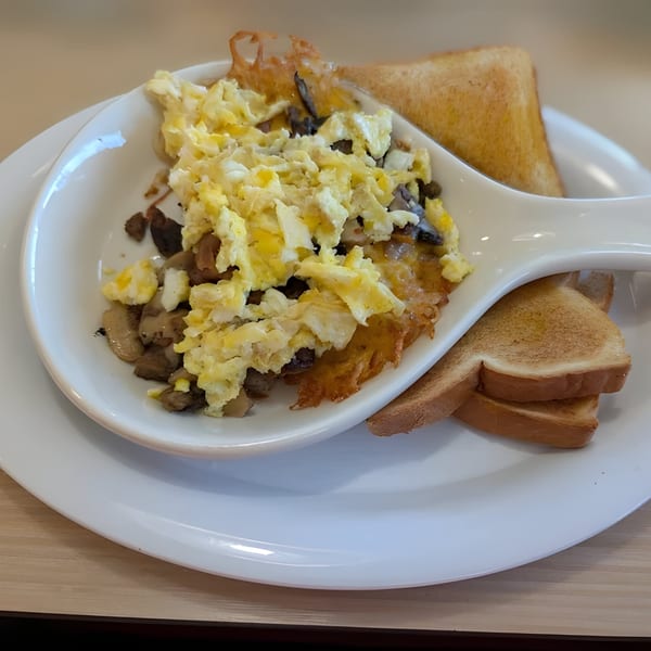 Scrambled eggs with mushrooms and onions served in a white dish with two slices of toast.