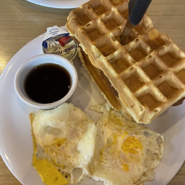 A waffle, two fried eggs, syrup, and butter on a white plate at That Flippin' Egg.