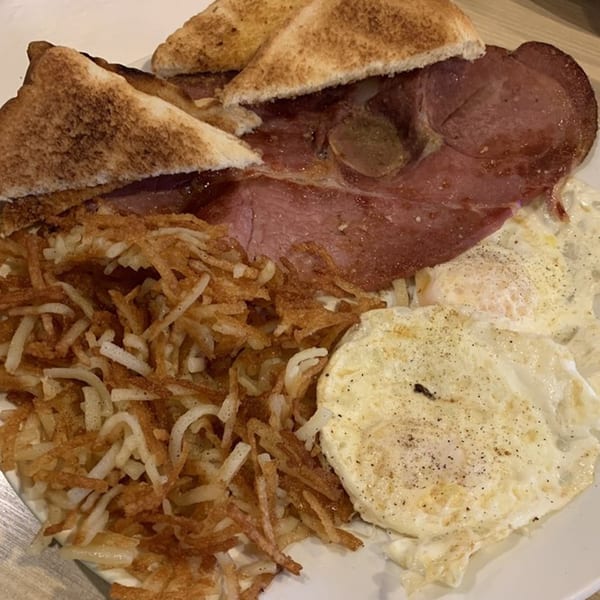 A breakfast plate with ham, hash browns, two fried eggs, and toast from That Flippin' Egg.
